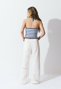 Top de tubo de ganchillo a rayas en azul marino y blanco, combinado con pantalones anchos blancos que presentan detalles de encaje en el dobladillo y bolsillos de parche.