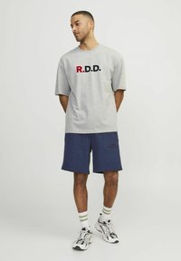 Pelēks kokvilnas T-krekls ar "R.D.D." grafiku sarkanā un tumši zilā krāsā, apvienots ar tumši zilām šortiem. Modelis valkā svītrainas baltas un zaļas zeķes un sporta apavus.