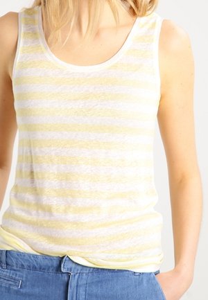 Débardeur blanc sans manches à rayures horizontales jaune pâle, porté avec un pantalon bleu, montrant le haut du torse et les bras.