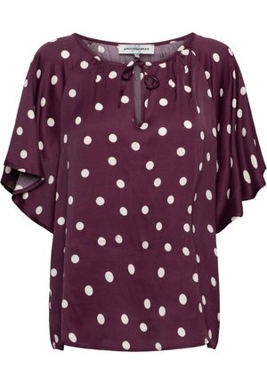 Lila blouse met korte mouwen, witte stippen, ronde hals en een kleine striksluiting aan de voorkant.