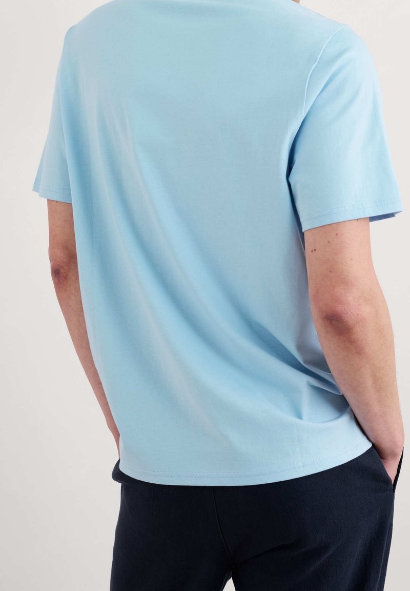 T-shirt en coton bleu clair avec un col rond et des manches courtes. Le design est simple, sans embellissements visibles.