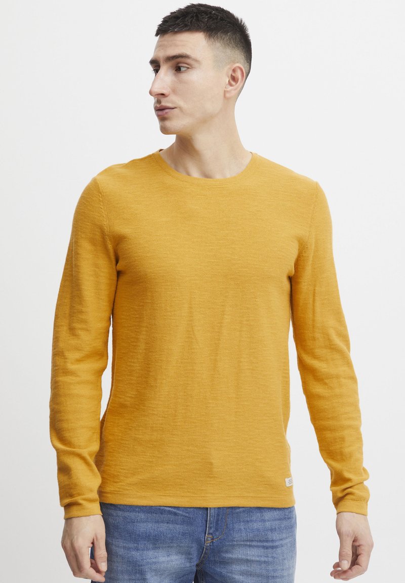 Długoobranżowa koszulka crew neck w kolorze musztardowym. Wykonana z miękkiego, strukturalnego materiału o luźnym kroju. Posiada małą metkę z logo przy dolnym brzeg.