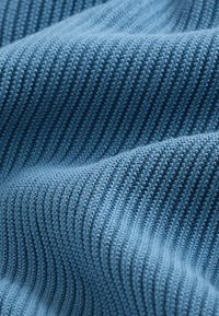 Blått stickat tyg med vertikala ränder och en slät textur, med synliga sömmar och ett mjukt, flexibelt fall.