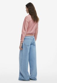 Helles rosa cropped Jeansjacke mit sichtbaren Nähdetails, kombiniert mit weit geschnittenen hellblauen Jeans, die über Hosentaschen und eine ausgeblichene Textur verfügen.