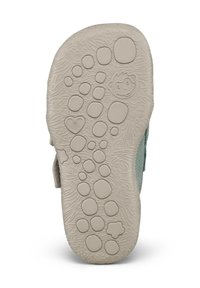 Suola di una scarpa da bambino con motivi circolari in rilievo, un cuore, un fiore e una faccia di scimmia su una superficie beige testurizzata.