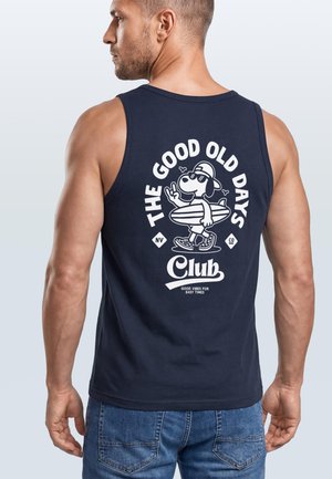 Mann trägt ein marineblaues Tanktop mit weißem Druck eines Hundes, der ein Surfbrett hält, und dem Text „The Good Old Days Club“ auf dem Rücken.