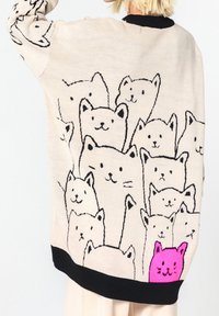 Maglione a maglia beige con un design giocoso di molteplici facce di gatti neri, che presenta un vivace gatto rosa in basso. Rifiniture nere.