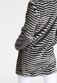 Cappotto in pelliccia sintetica con motivo a righe bianche e nere, caratterizzato da una texture morbida e maniche lunghe, progettato con una silhouette leggermente svasata.