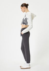 Korte witte hoodie met grafische print; zwarte joggingbroek met elastische manchetten; witte sneakers met lichtbruine zolen; zachte katoenen stof.