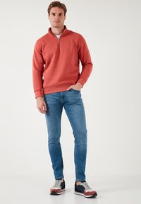 Sudadera roja con cuello con cremallera, combinada con vaqueros slim-fit azules y zapatillas multicolor. Diseño sencillo con puños y dobladillo acanalados.