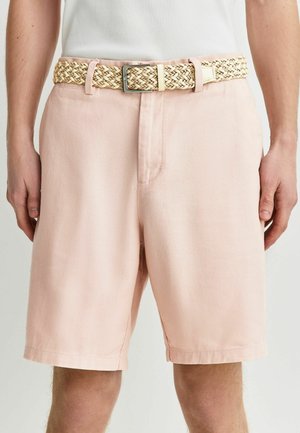 Jasnoróżowe szorty do kolan z tkaną beżową paskiem i srebrną klamrą, noszone z białym topem bez rękawów.