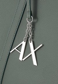 Zelena teksturirana umjetna kožna torba sadrži srebrne metalne akcenta i lanac s dva oznaka slova, "A" i "X".