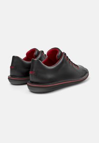 Scarpe di pelle nera con accenti rossi, lacci tondi, una texture liscia e una striscia rossa a contrasto lungo la suola.