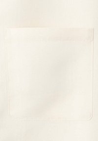 Gros plan d'une poche carrée, unie, en tissu écru, cousue sur un fond texturé écru assorti.