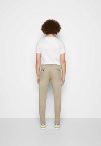 Chinos beige con un diseño ajustado, bolsillos traseros y una textura sutil, combinados con una camisa de rayas de manga corta y zapatillas coloridas.