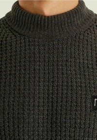 Grau-dunkler gestrickter Pullover mit hohem Kragen, einem strukturierten Muster und einem kleinen schwarzen Etikett auf der linken Seite.