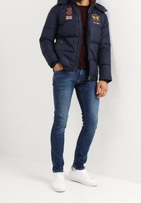 Námořnická prošívaná bunda s kapucí, předním zipem, červenými akcenty a vyšívanými detaily. Nositelná přes vínovou košili a úzké džíny s bílými teniskami.