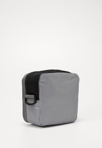 Borsa rettangolare grigia realizzata in tessuto liscio, con parte superiore nera, zip laterale e un piccolo anello per attacco. Design compatto.