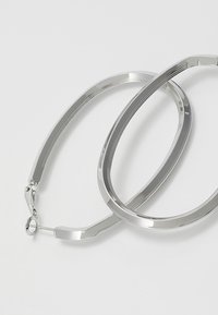 Sidabriniai žiedai ausims, turintys elegantišką, pailgą ovalo formą, poliruotą paviršių ir tekstūruotas kraštus, suteikiančius papildomo akcento.