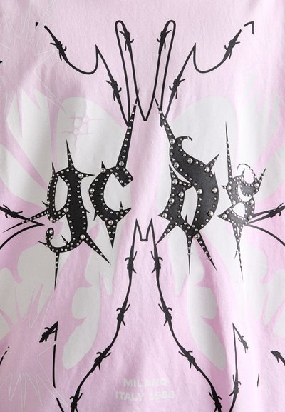 T-shirt en tissu rose clair avec un design graphique noir comportant des piques et des strass. Un texte en bas indique "MILANO ITALY 1988."
