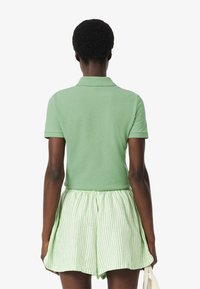 Polo vert avec un col, associé à un short rayé vert clair et blanc. La chemise a des manches courtes et une coupe décontractée.