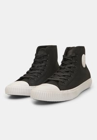 Crne visoke tenisice od teksturirane platnene tkanine, s bijelim gumiranim vrhom i prugastim potplatom; sadrže crne vezice i reljefni logo.