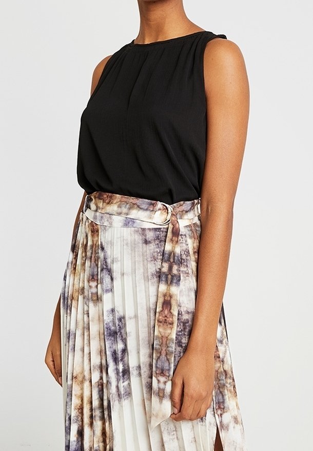 Top sans manches noir avec un col plissé, assorti à une jupe fluide multicolore avec une taille à nouer et de nombreux motifs en tissu.