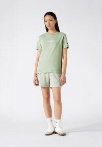 Camiseta de algodón de color verde claro con "LOS ÁNGELES" impreso en blanco, combinada con pantalones cortos a juego; ofrece un ajuste relajado y una textura suave.