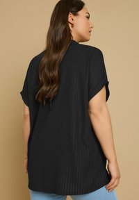 Top corto a maniche corte di colore nero, realizzato in tessuto texturizzato a coste e con una vestibilità rilassata. Presenta maniche arrotolate e un orlo curvo, abbinato a jeans azzurri chiari.