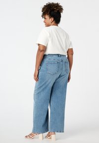 Lichtblauwe wijdvallende jeans met een hoge taille, vijf zakken en een rafelige zoom. Gecombineerd met een witte t-shirt met korte mouwen.