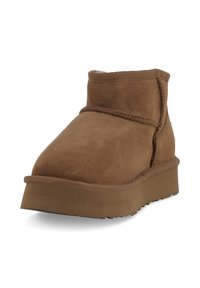 Stivale alla caviglia in suede marrone con suola spessa, cuciture visibili e morbido rivestimento interno, mostrato da un angolo leggermente inclinato su uno sfondo bianco.