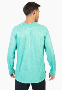 Langærmet skjorte i en lys turkis farve, med et struktureret stof, rund kant og et logo trykt lodret på ryggen.