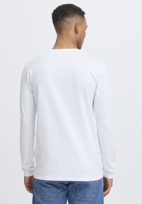 Long-sleeve white shirt made of soft cotton, featuring a classic round neckline and a relaxed fit, paired with blue denim jeans.