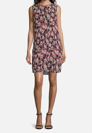 Ærmeløs knælange plisseret kjole med rød, hvid og sort blomsterprint, båret med sorte højhælede sandaler med ankelrem.