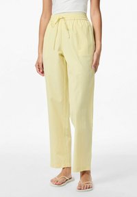 Lichtgele gestreepte broek met een elastische tailleband en koord. Rechte pasvorm met subtiele textuur. Draagt flip-flops.