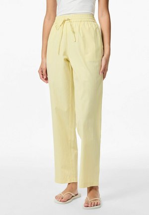 Pantalons rayés jaune clair avec une taille élastique et un cordon de serrage. Coupe droite avec une texture subtile. Portés avec des tongs.