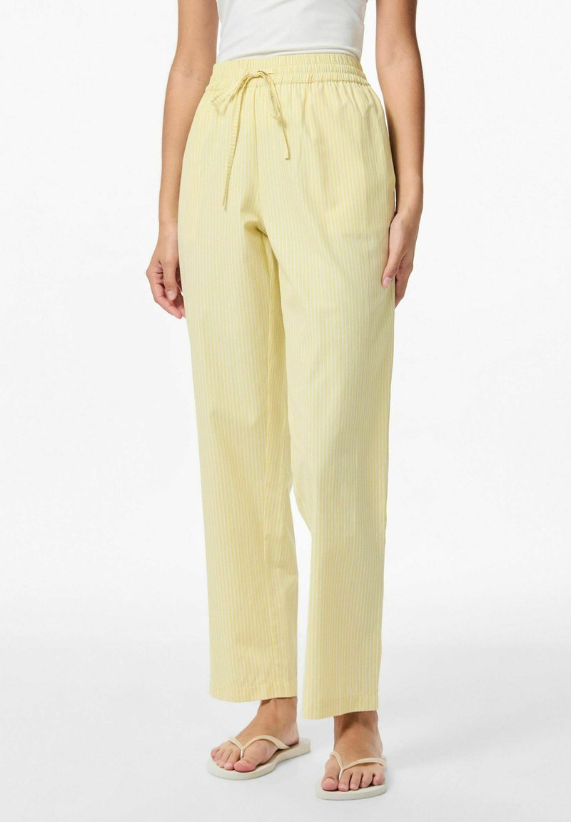 Lichtgele gestreepte broek met een elastische tailleband en koord. Rechte pasvorm met subtiele textuur. Draagt flip-flops.