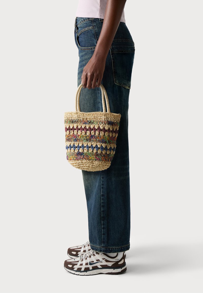 Bolso de paja trenzada con patrones coloridos en tonos de púrpura, verde y azul; cuenta con dos asas resistentes y una forma redondeada.