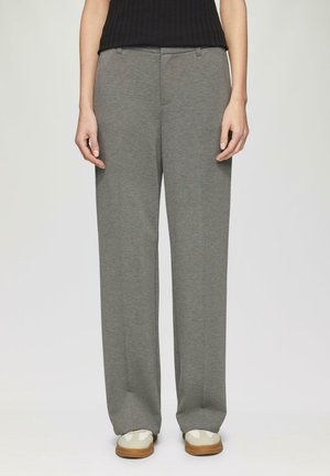 Pantalons gris sur mesure en tissu doux, avec une coupe droite, des poches avant et une texture lisse. Associés à des baskets blanches.
