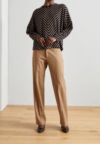 Svetr s černobílými pruhy, pletený, s volným střihem, v kombinaci s béžovými kalhotami na míru a tmavě hnědými botami na vysokém podpatku se špičatou špičkou.