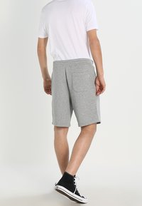 Shorts en coton gris avec une ceinture élastique et une poche arrière, associés à un t-shirt blanc uni et des baskets montantes noires.