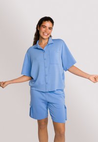 Lichtblauw bijpassend set bestaande uit een kortemouw knoopshirt met een zak en shorts met zijzakken, gemaakt van zachte stof.