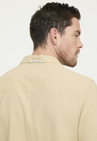 Beige overhemd met korte mouwen van een gestructureerde stof, met een puntige kraag en een klein label op de achterkant met "LEE COOPER" branding.