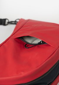 Borsa in poliestere rossa con fodera interna grigia, dotata di una tasca con zip e di una tracolla resistente. Il design è elegante e pratico.