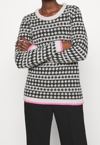 Strickpullover mit schwarz-weißen geometrischen Mustern, einem rundem Ausschnitt und pinken Akzenten an den Bündchen und am Saum.