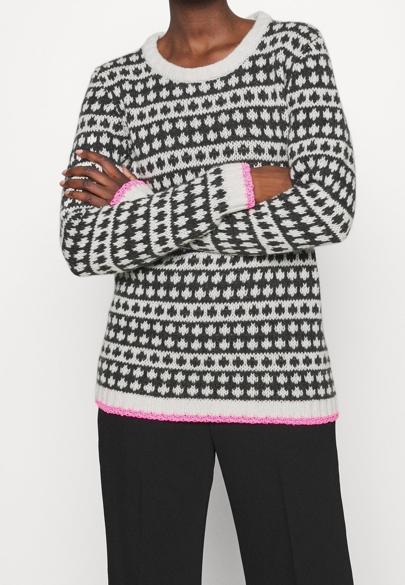 Strickpullover mit schwarz-weißen geometrischen Mustern, einem rundem Ausschnitt und pinken Akzenten an den Bündchen und am Saum.