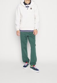 Vit fleece-hoodie med ficka fram, gröna sweatpants och färgglada sneakers. Har randiga lager under hoodien.