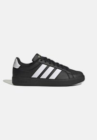 Baskets Adidas basses noires avec trois bandes blanches, semelle noire, lacets et languette argentée au talon, vues de profil sur un fond clair.