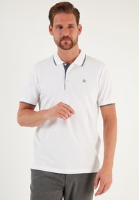 Bílá polo tričko s krátkými rukávy, kontrastním šedým límečkem a manžetami, tříknoflíkovým zapínáním a malým vyšívaným logem.