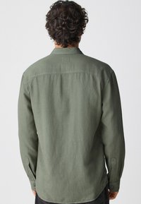 Olivgrünes Langarmhemd mit Button-Down-Kragen, feiner Textur und Manschetten mit einem Knopf. Verfügt über eine Schulter-naht auf der Rückseite.